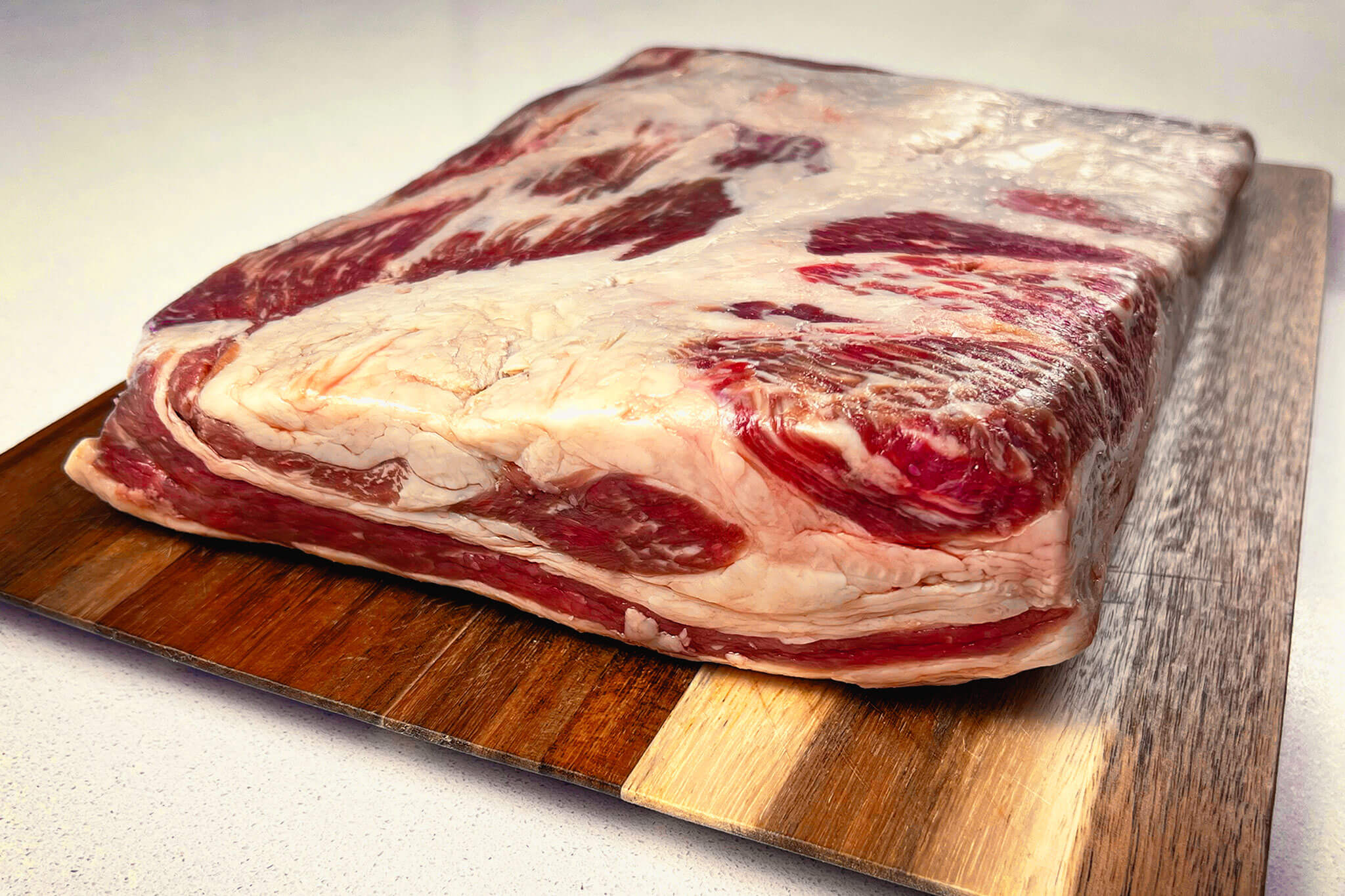 Fresh raw beef navel cut with thick fat layer on wooden butcher board for premium meat product photography