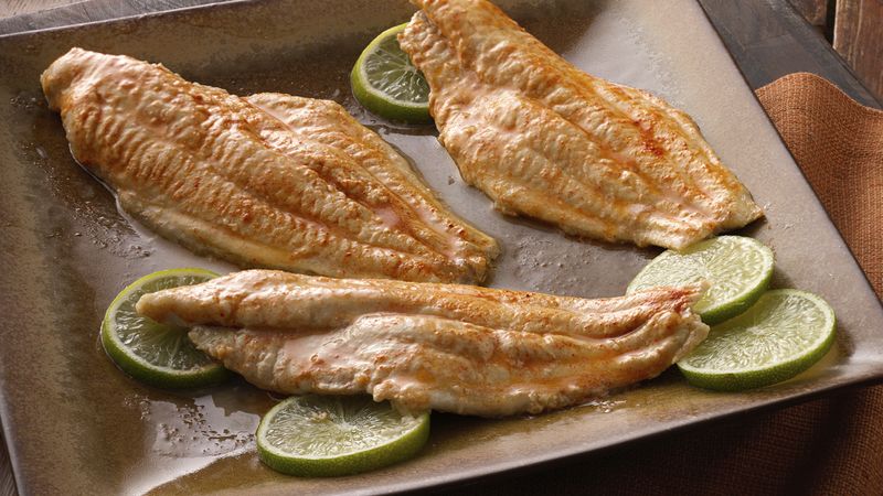 Golden baked fish fillets with fresh lime slices on metal baking tray for healthy seafood meal photography