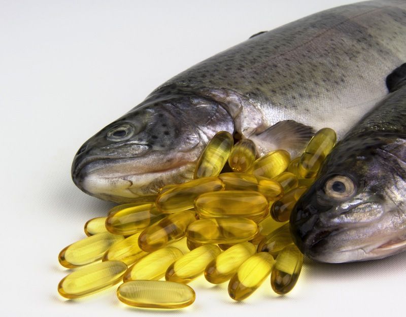 Fresh whole fish with golden omega 3 fish oil supplement capsules on white background for health product photography