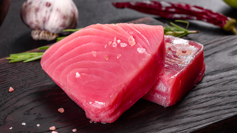 Fresh raw tuna steaks with sea salt rosemary garlic and red chili on dark wooden board for premium seafood photography