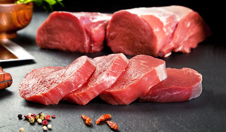 Assorted fresh raw meat cuts and slices on dark slate surface with mixed peppercorns and dried chili for butcher shop