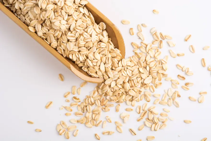 Rolled oats spilling from wooden scoop on white background for healthy whole grain cereal product photography